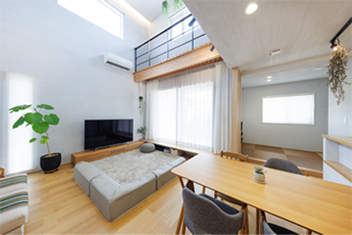 開放的な吹き抜けとハイサイドライト（高窓）から、明るい自然光が降り注ぐリビング空間。