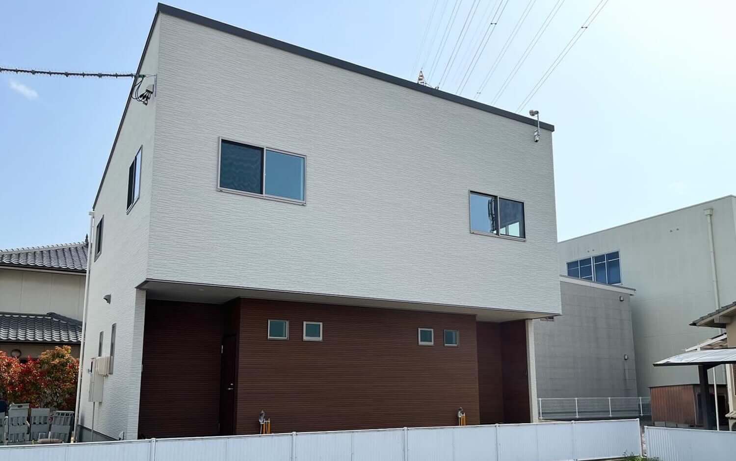 しっぽハウスの外観。2階建てのモダンな住宅で、上部は明るいグレーのサイディング、下部は茶色のパネル張り